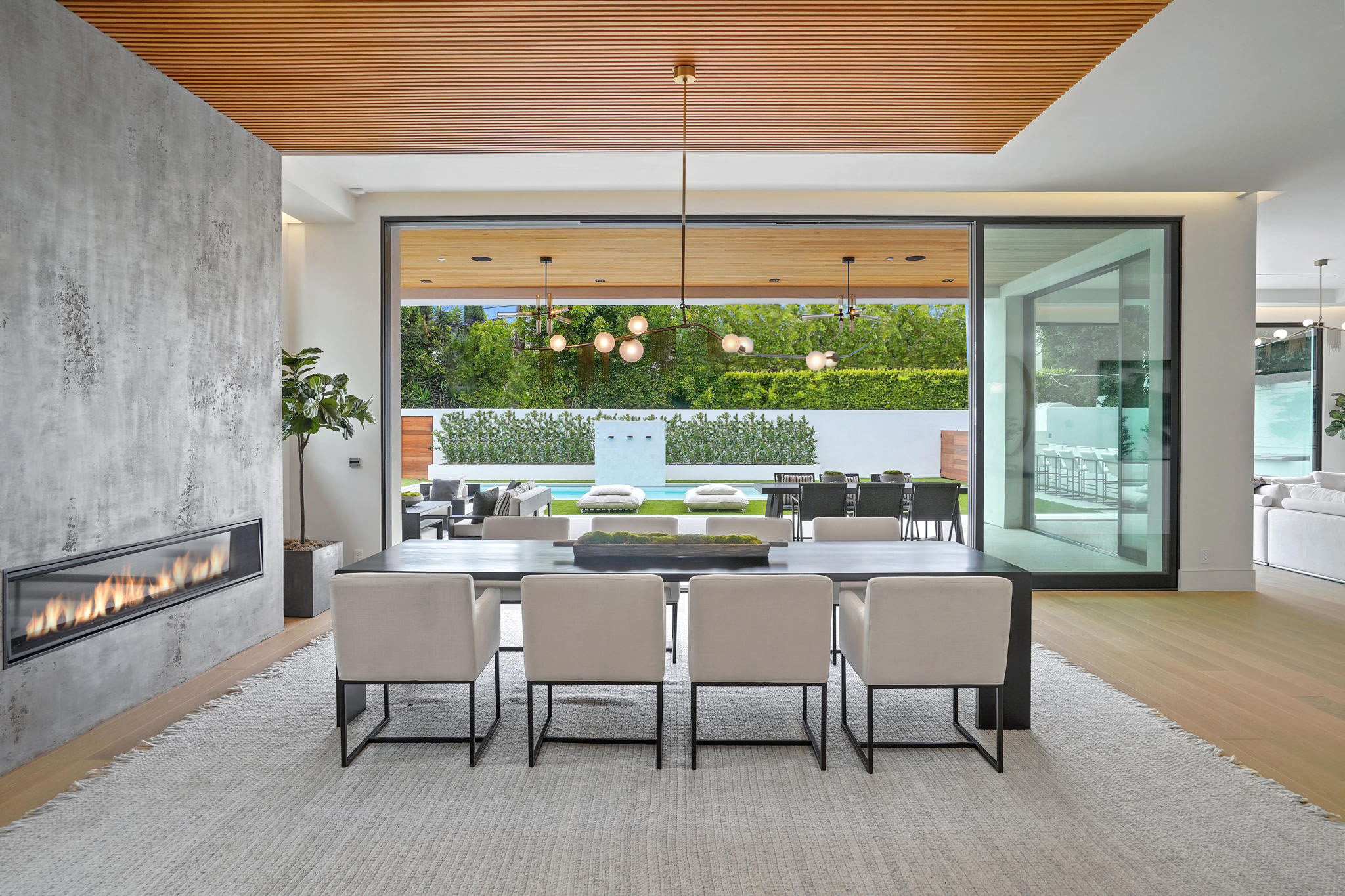 Modern Beverly Hills luxury dining room by Lori Dennis with fireplace, wood ceiling, sliding glass doors, and backyard view.